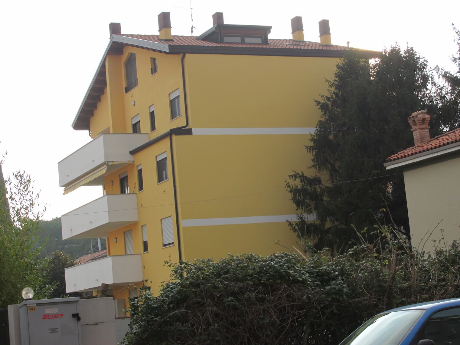 Un edificio giallo con balconi e un'auto blu parcheggiata di fronte