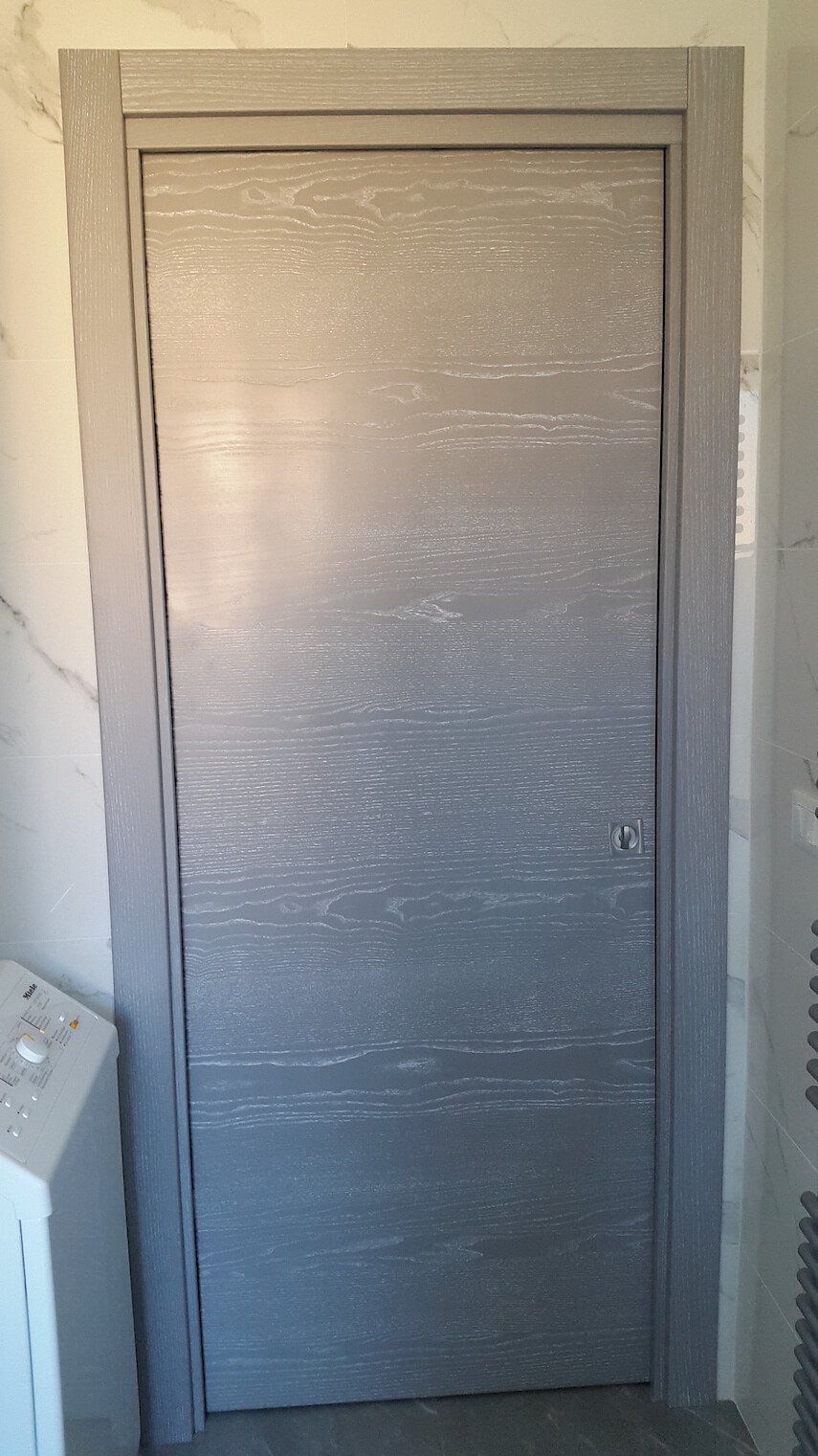 Una porta grigia si trova in una stanza accanto a una lavatrice.