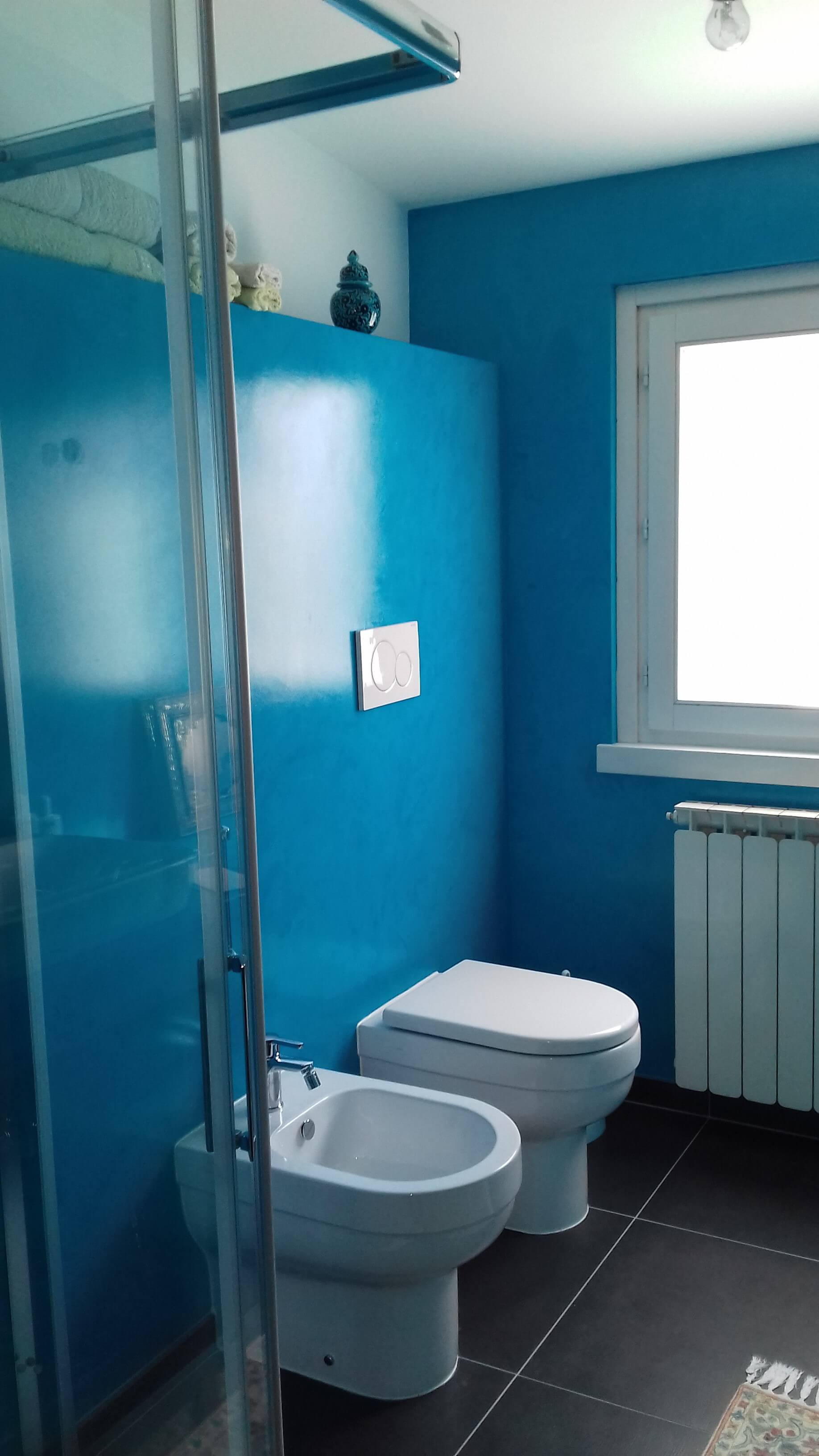 Un bagno con pareti blu, due water, un bidet e una finestra.