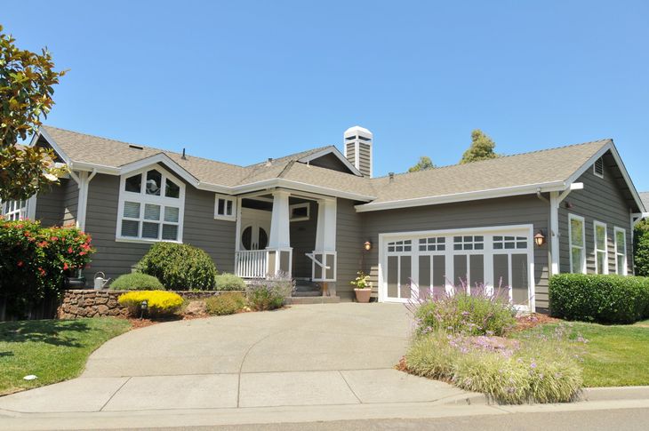 Gray suburban house with stone accents, large driveway, and landscaped front yard under a clear sky