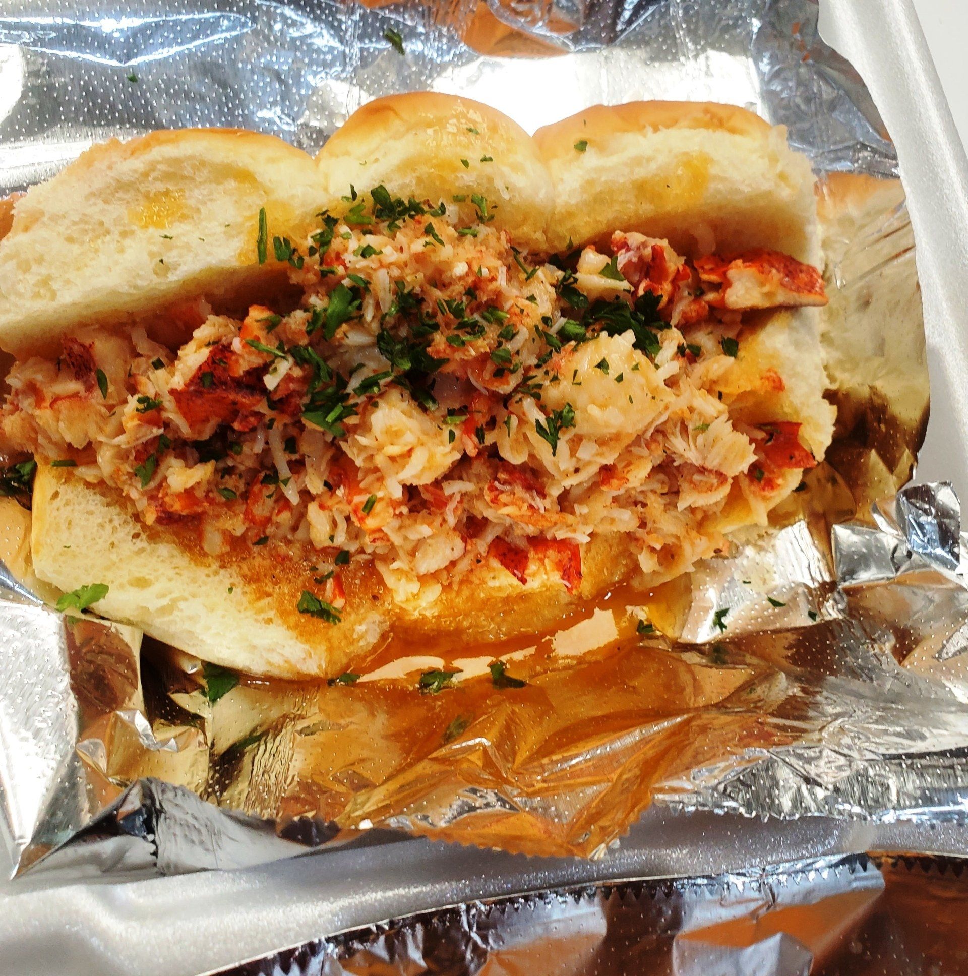 Lobster roll on a toasted bun, filled with lobster meat and sprinkled with parsley, served on foil.
