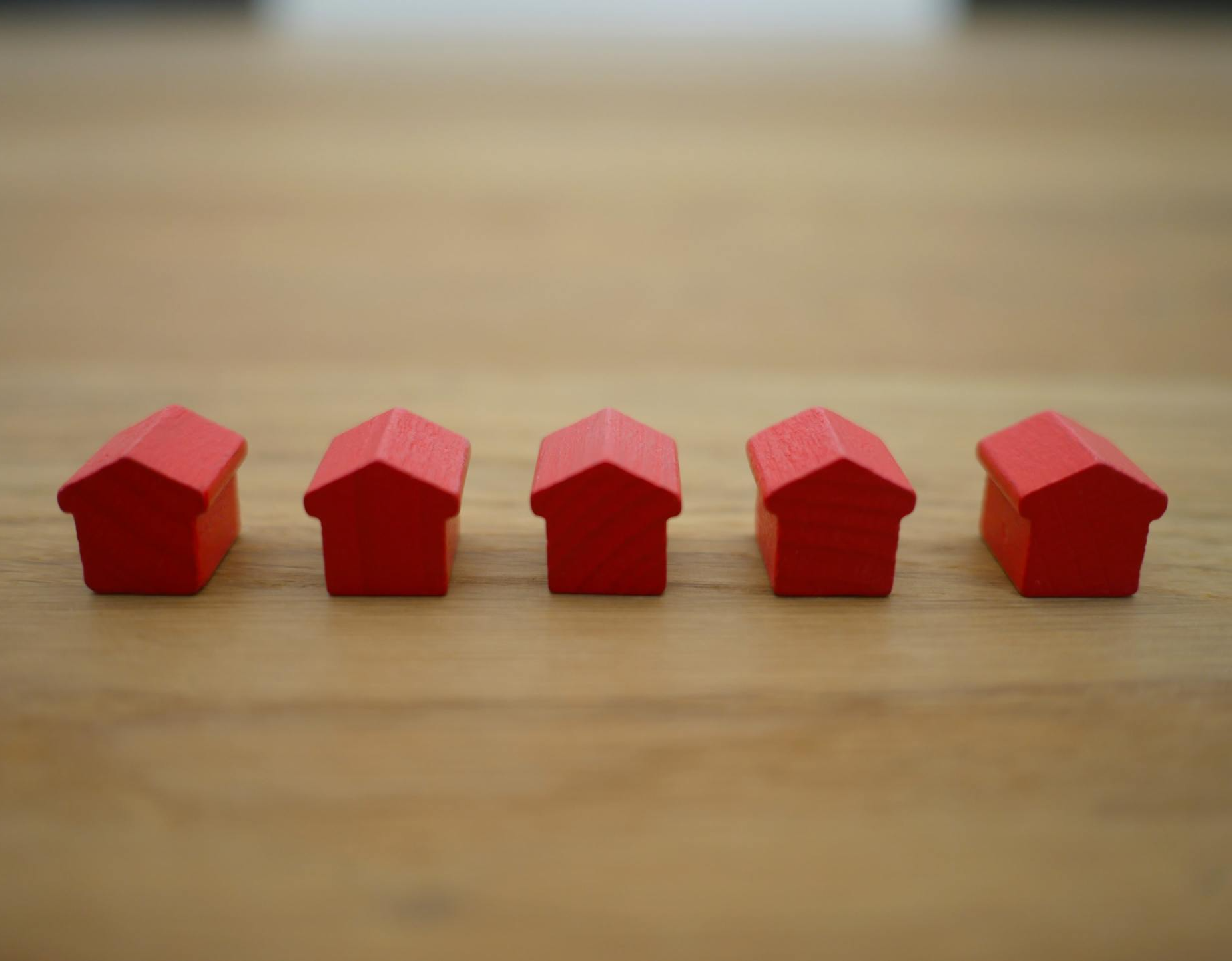 Five small red house-shaped blocks lined up on a wooden surface.