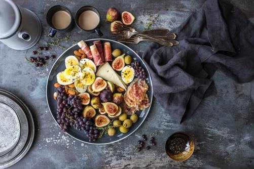 Une assiette de nourriture avec des œufs, des raisins, des figues, des olives et du fromage sur une table.