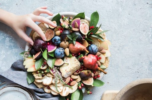 Une personne prend une prune dans une assiette de fruits de saison du mois de septembre et de fruits à coques.