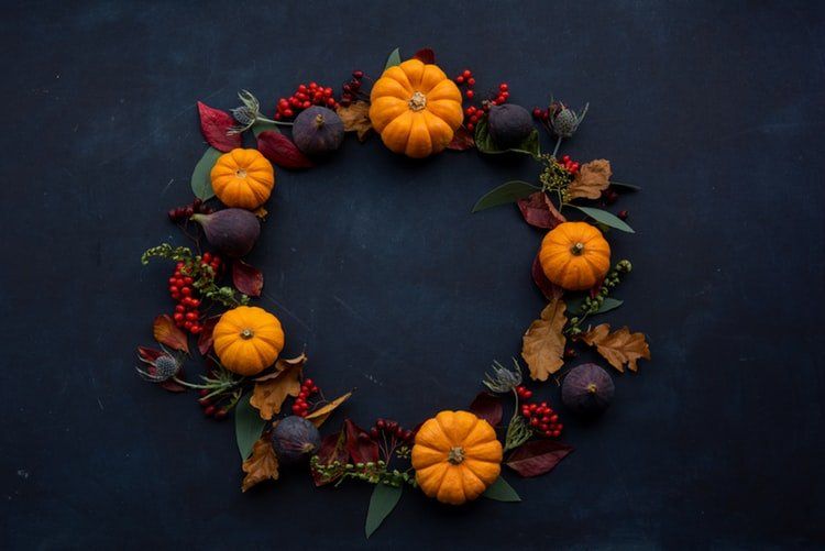 Une couronne composée de citrouilles, de feuilles, de baies et de figues sur fond noir.