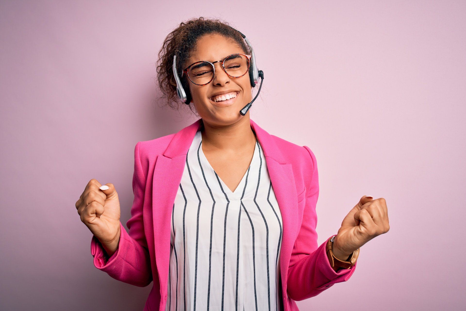A woman wearing a pink jacket and glasses is wearing a headset.