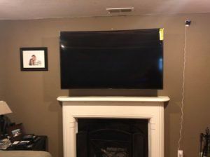 Large TV mounted above a fireplace, brown wall, small picture to the left.