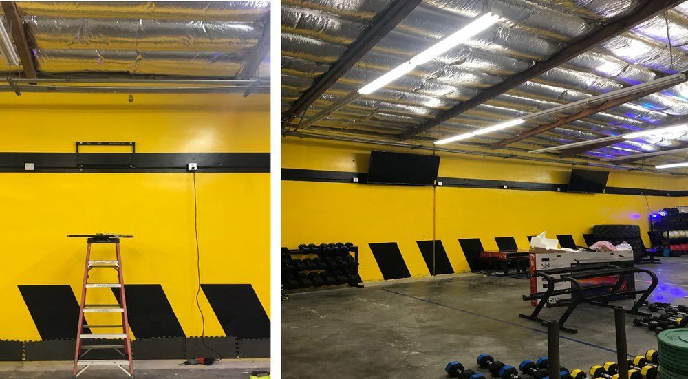 Yellow and black gym interior with weights, equipment, and a ladder against the wall.