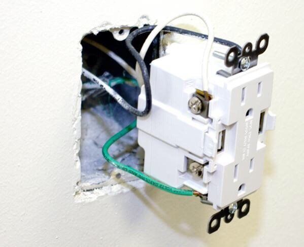 White electrical outlet in wall cavity with black and white wires connected. Green grounding wire visible.