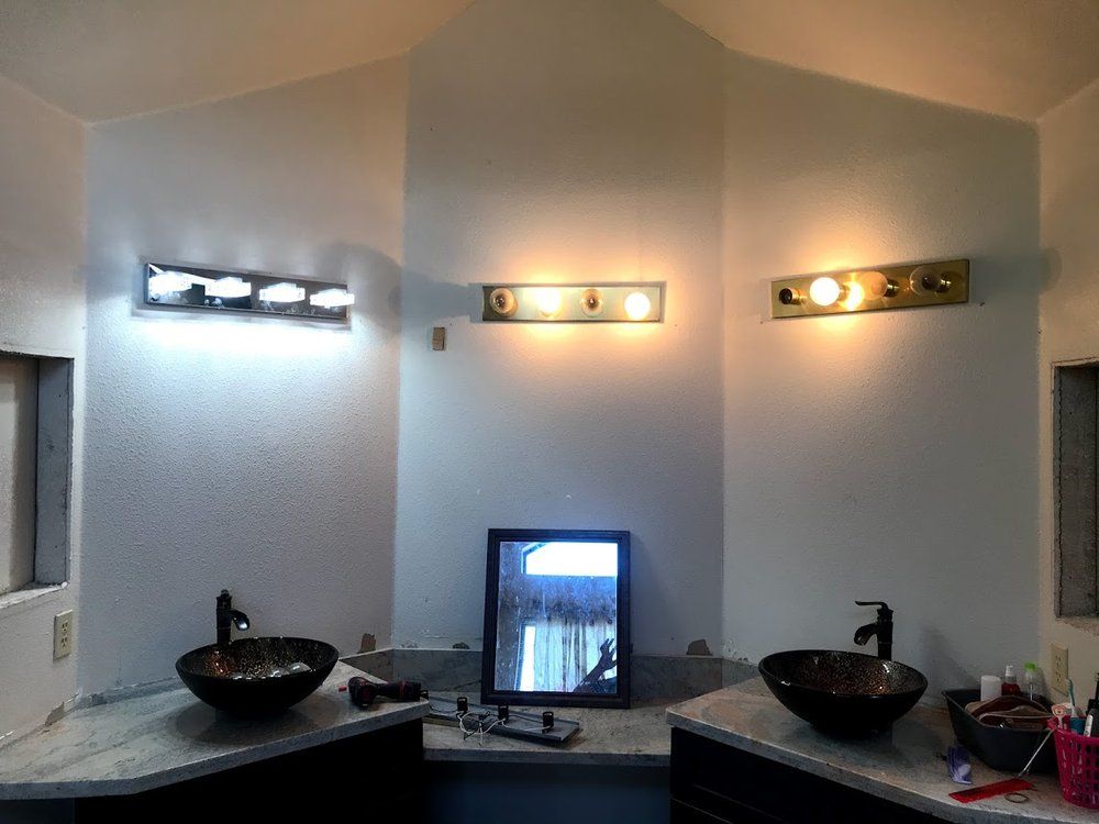Bathroom with three light fixtures above sinks, black bowl sinks, and a mirror.