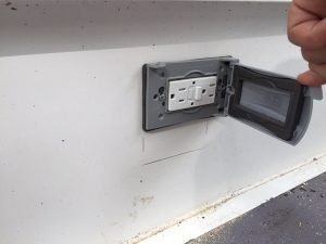 Outdoor electrical outlet with a weather-resistant cover being opened by a hand.