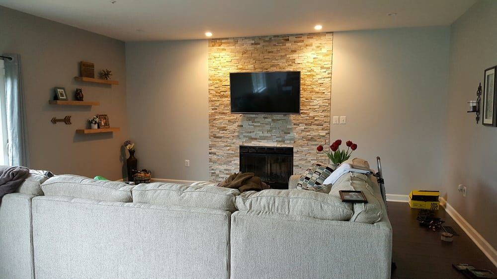 Living room with stone fireplace, TV, and sectional sofa; floating shelves on the left wall.