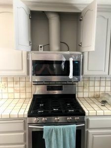Microwave above a gas stove in a kitchen; open cabinet doors reveal ventilation.