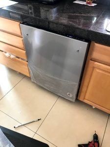 Stainless steel dishwasher installed between light wood cabinets, under a dark countertop.