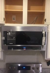 A stainless steel microwave installed under kitchen cabinets, above a matching stove. Power outlet visible.