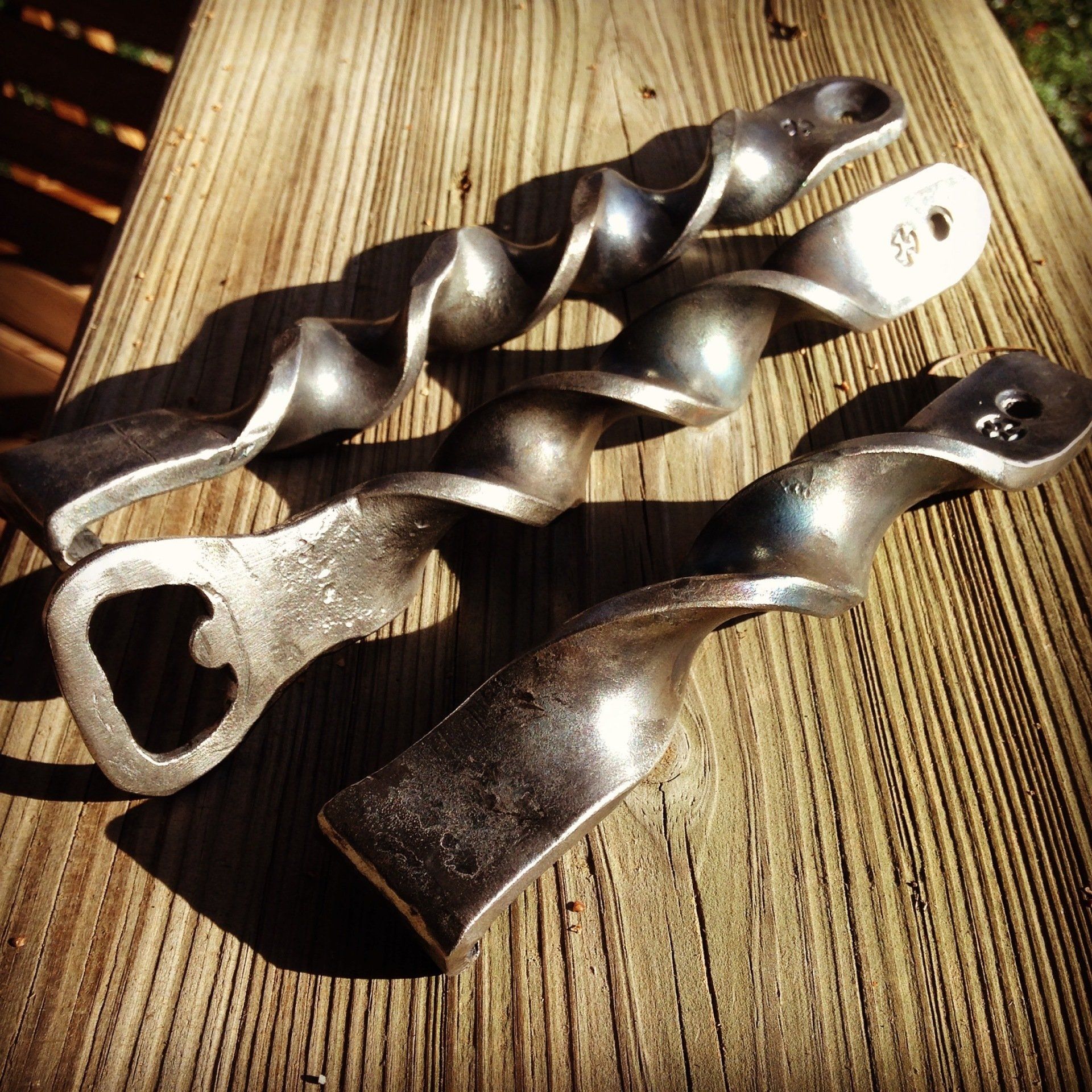 Three metal bottle openers are sitting on a wooden table