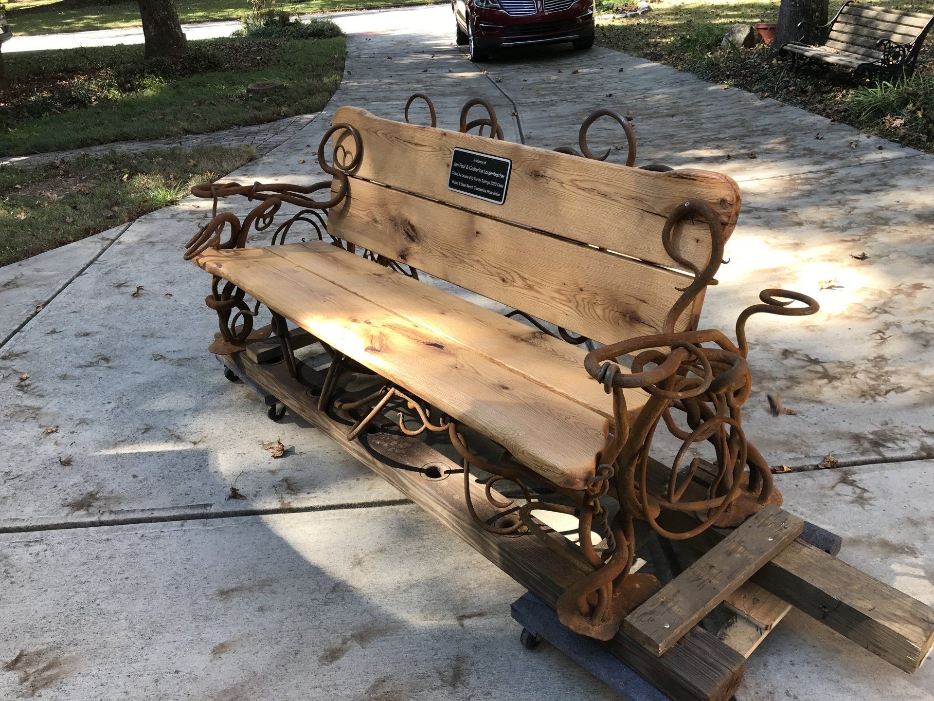 A wooden bench is sitting on a concrete surface next to a car.
