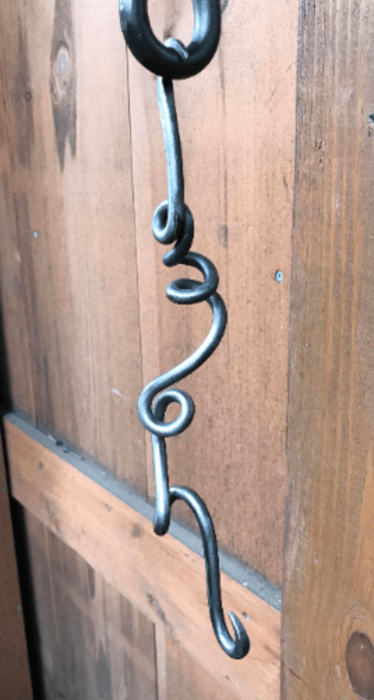 A close up of a metal hook hanging from a wooden wall.