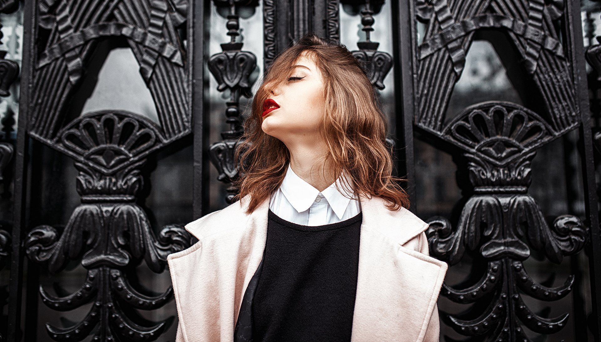 A woman is standing in front of a black gate with her eyes closed.