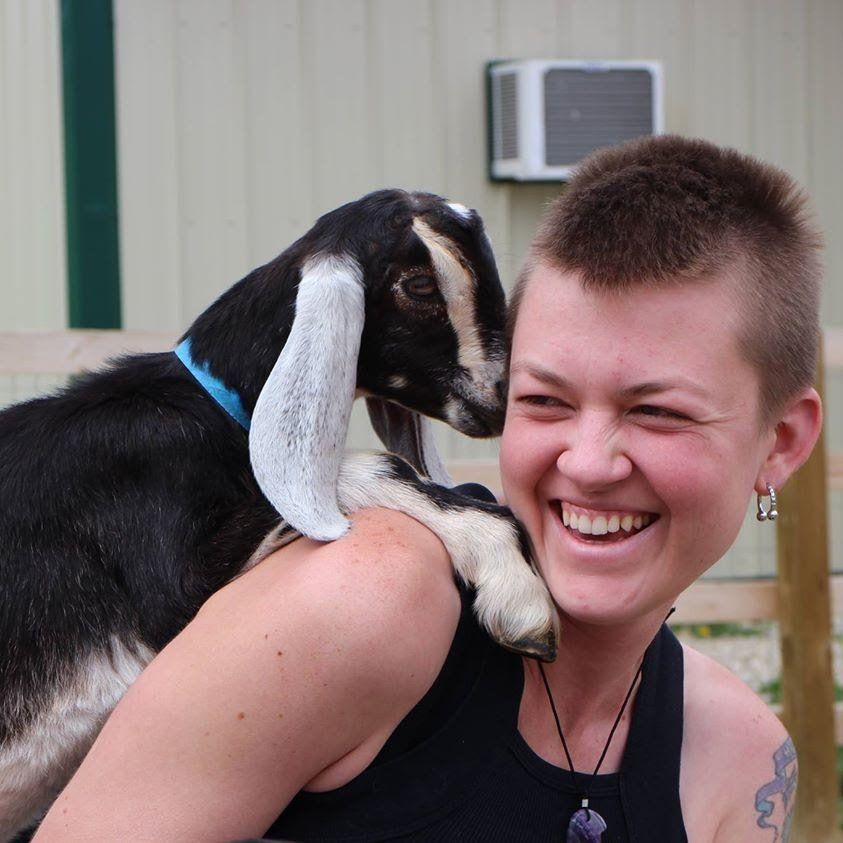 A woman is smiling while holding a goat on her shoulder
