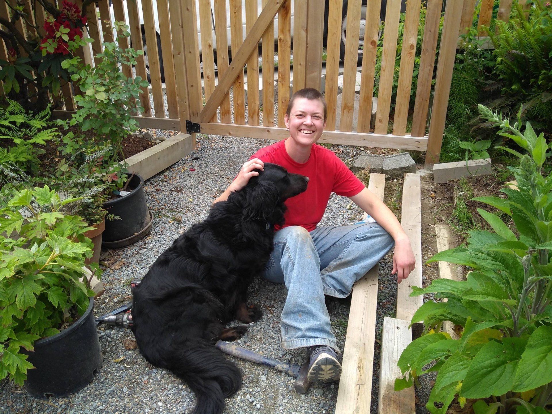 A man in a red shirt sits next to a black dog