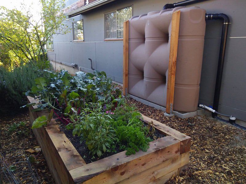 A brown water tank is sitting next to a wooden planter filled with plants.