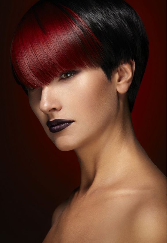 A woman with short black hair and red bangs is wearing purple lipstick.