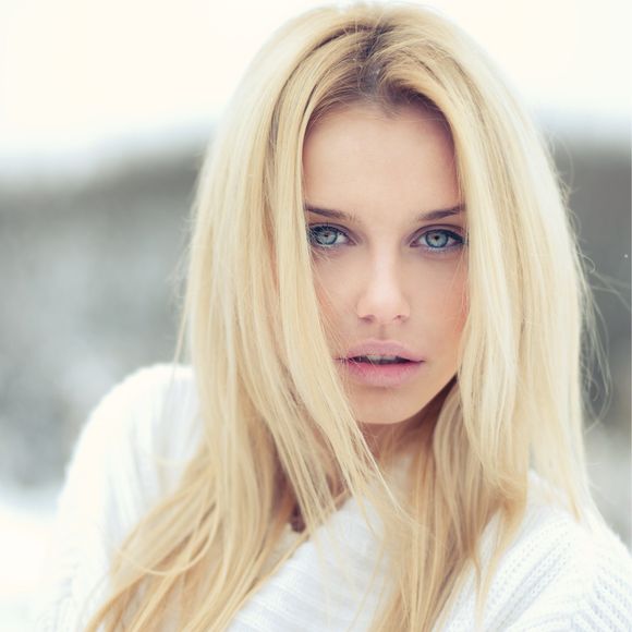 A woman with blonde hair and blue eyes is wearing a white sweater.