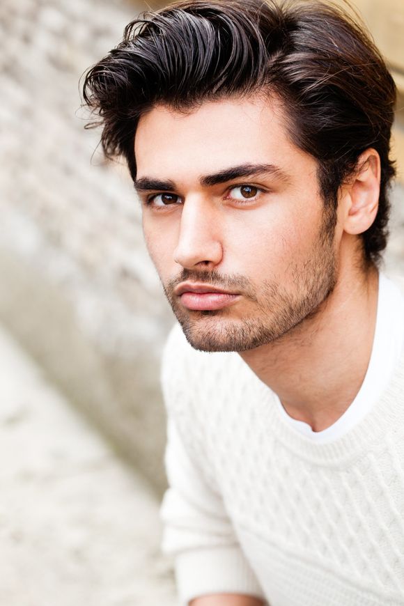 A man with a beard is wearing a white sweater and looking at the camera.