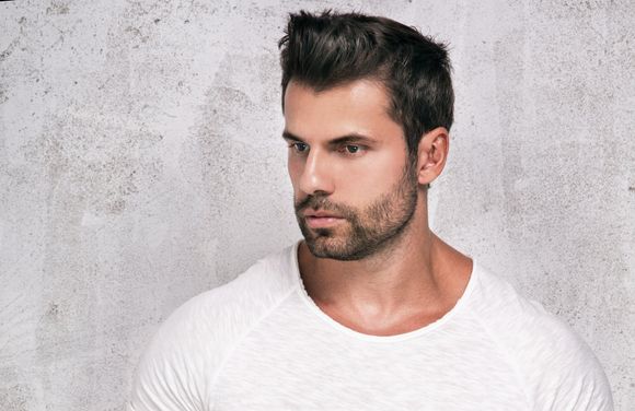 A man with a beard is wearing a white t-shirt and looking at the camera.