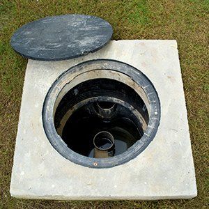 Open manhole in a concrete slab with the round cover resting beside it