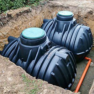 Two large black underground septic tanks installed in a dirt trench