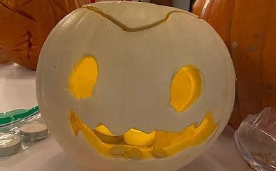 A white pumpkin with a yellow face carved into it is sitting on a table.