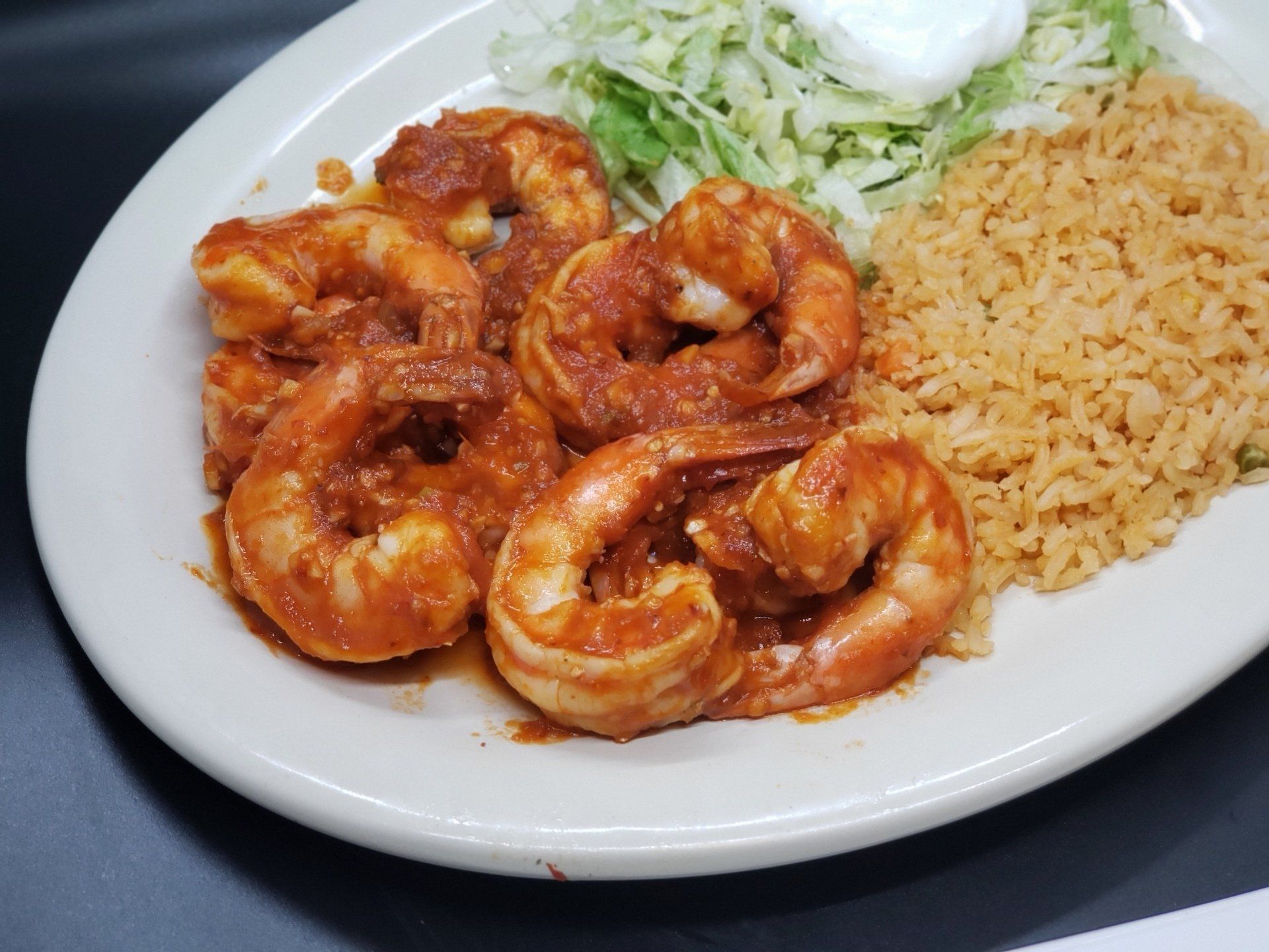 Shrimp in red sauce with rice, lettuce, and sour cream on a white plate.