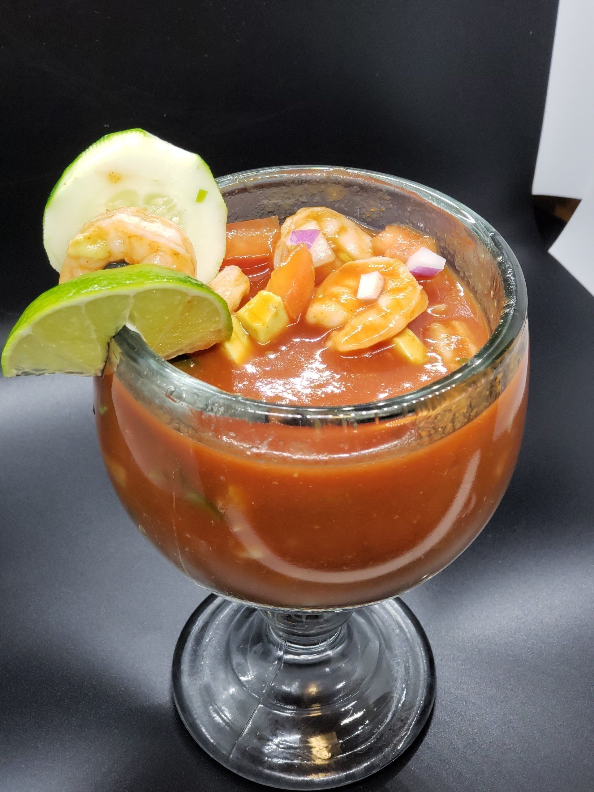 Shrimp cocktail in a glass, with lime and cucumber slices, set against a black background.
