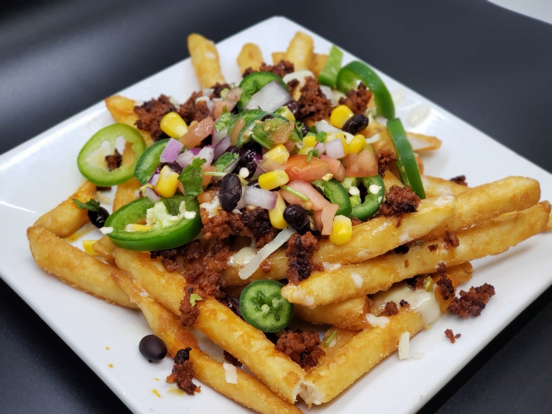 Loaded fries with toppings, including jalapeños, corn, black beans, salsa, and cheese on a white plate.