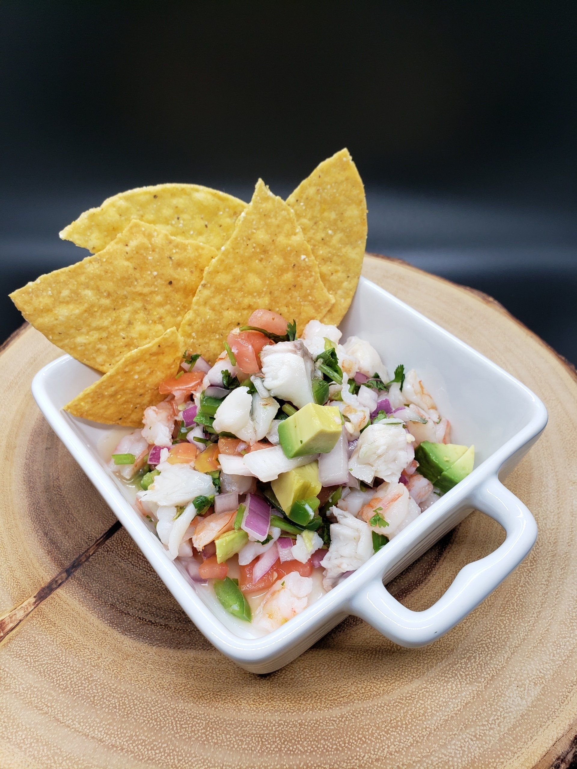 Ceviche with avocado, tomato, and red onion in a white bowl, served with tortilla chips.