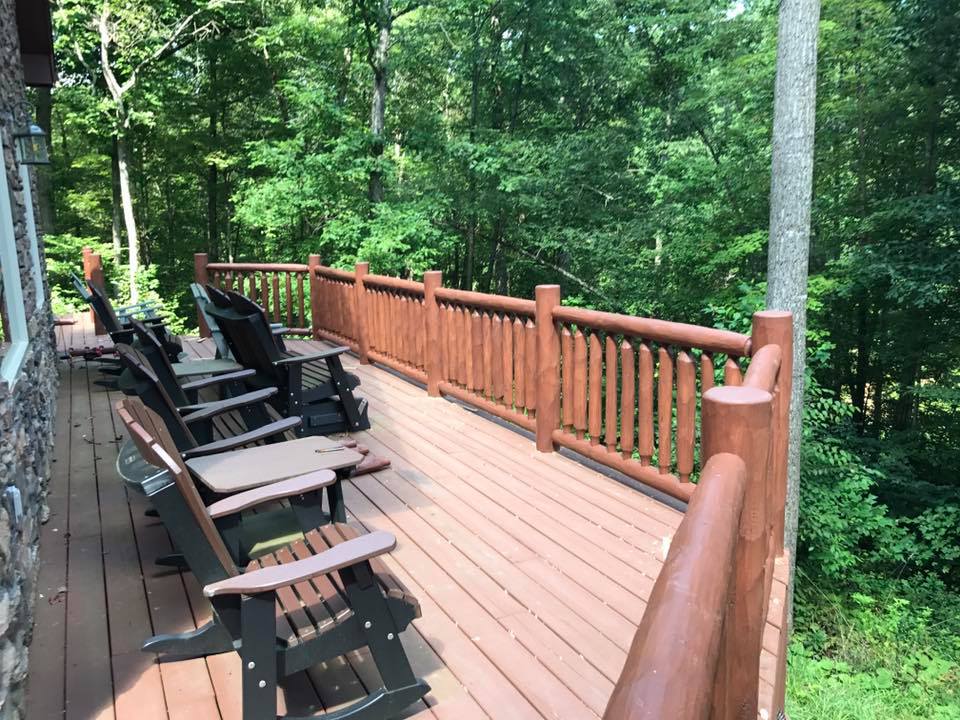 Wooden deck with black lounge chairs and railing overlooking a green wooded area