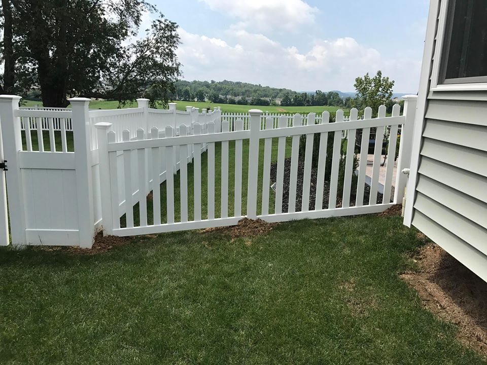 White vinyl fence and gate beside a house overlooking a grassy yard and pond