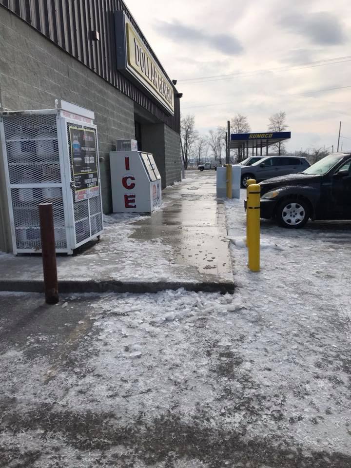Icy storefront sidewalk with a vending machine and parked car on a winter day