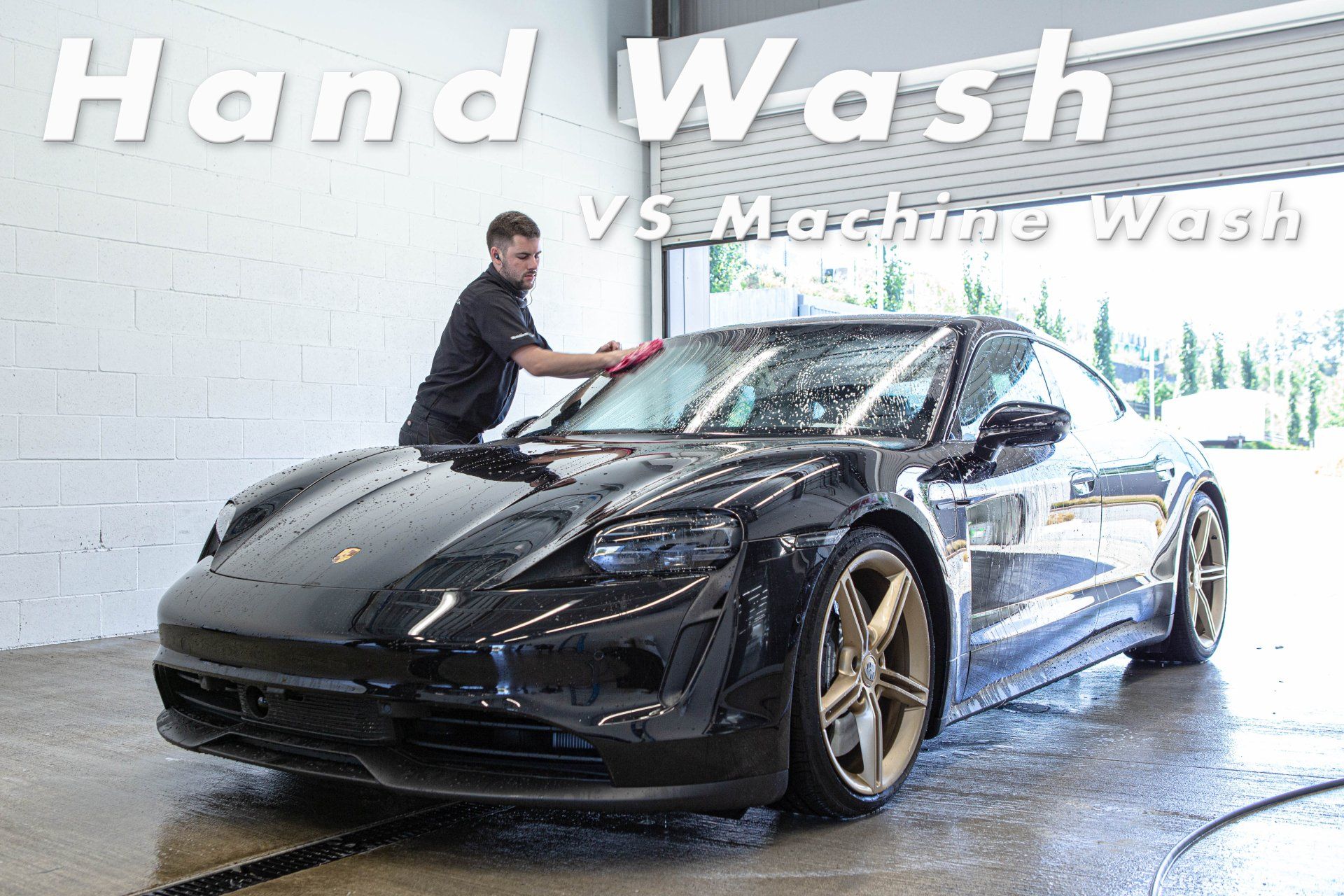 A man is washing a black sports car in a garage.