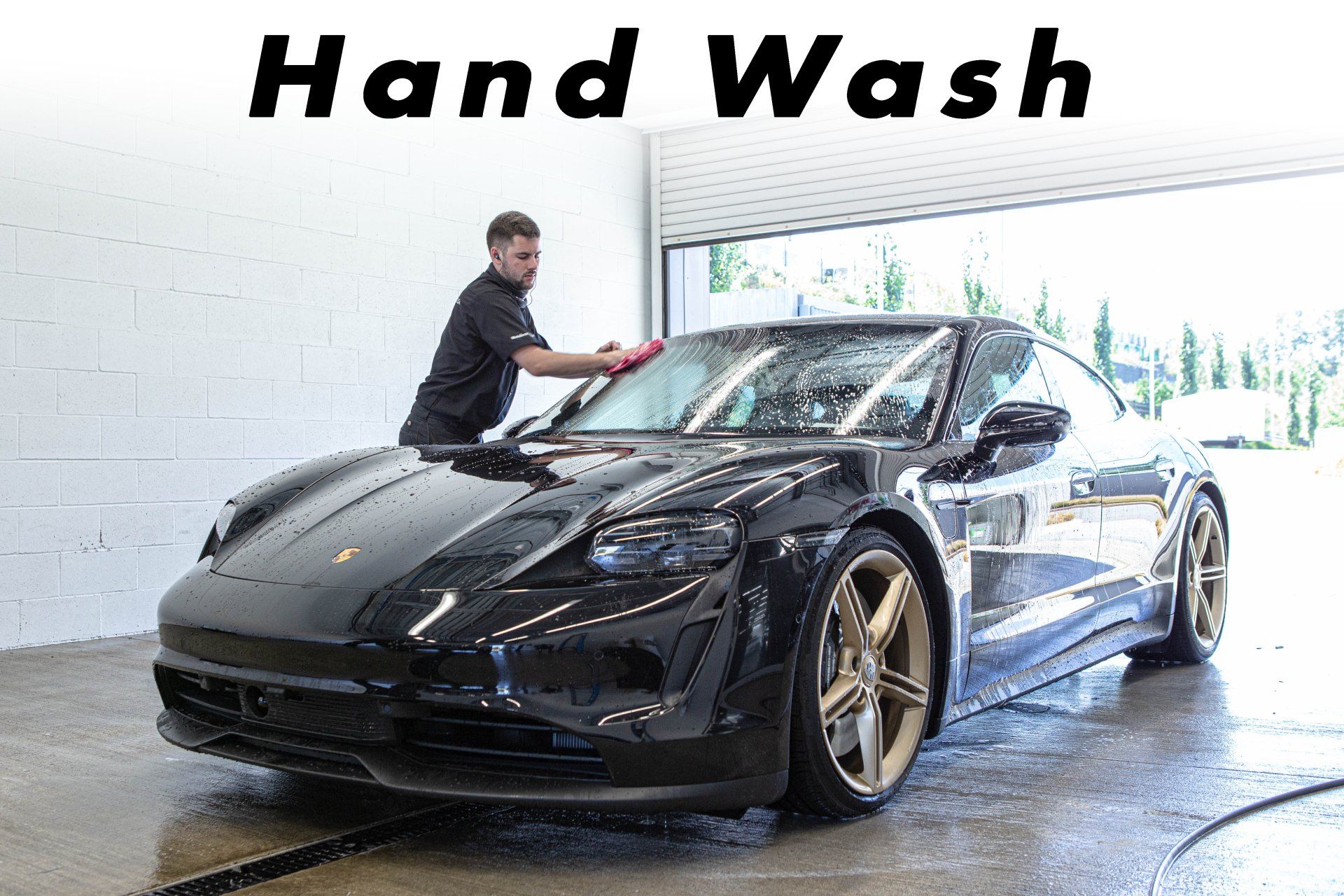 A man is washing a black sports car in a garage.