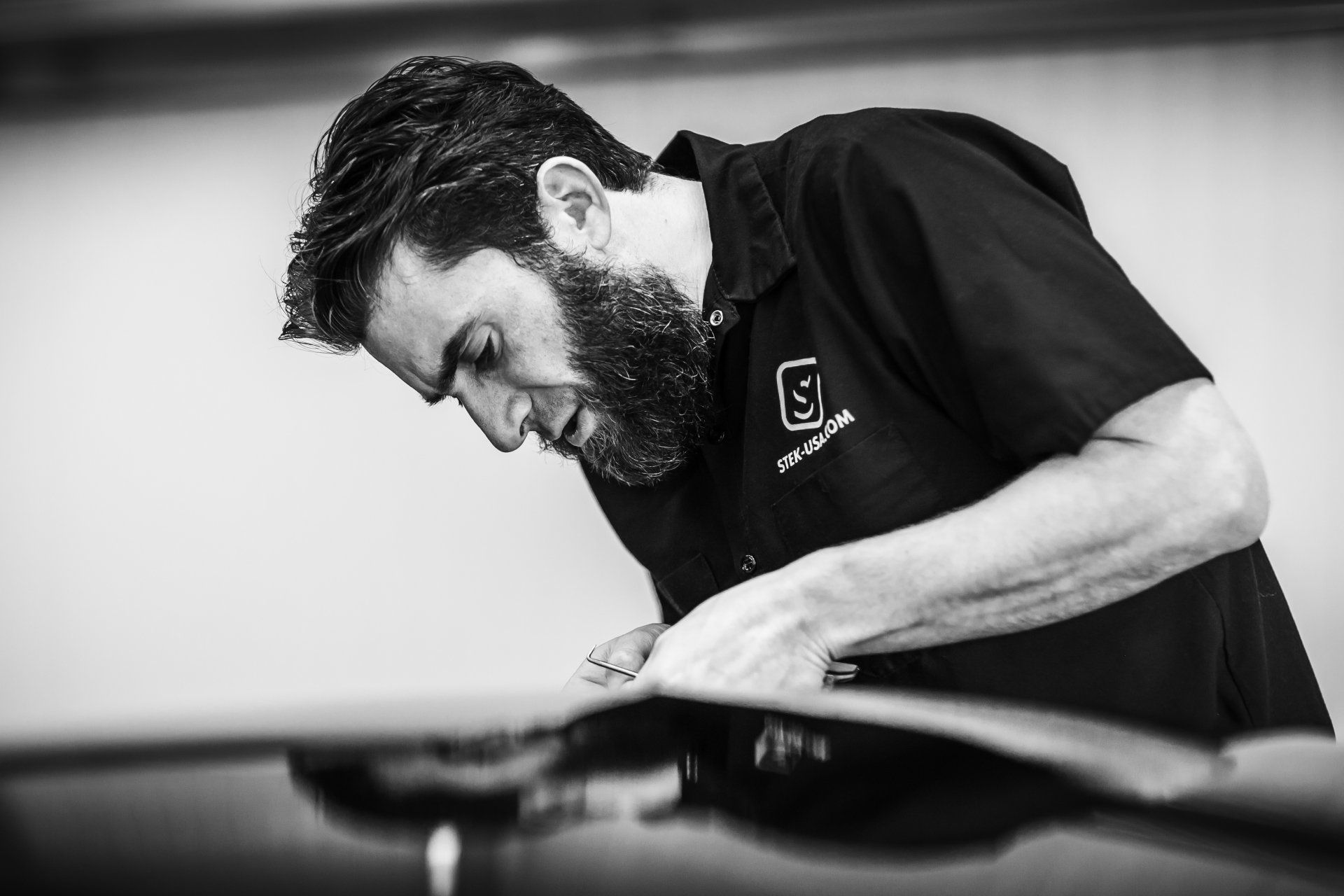 A man with a beard is working on a car in a black and white photo.
