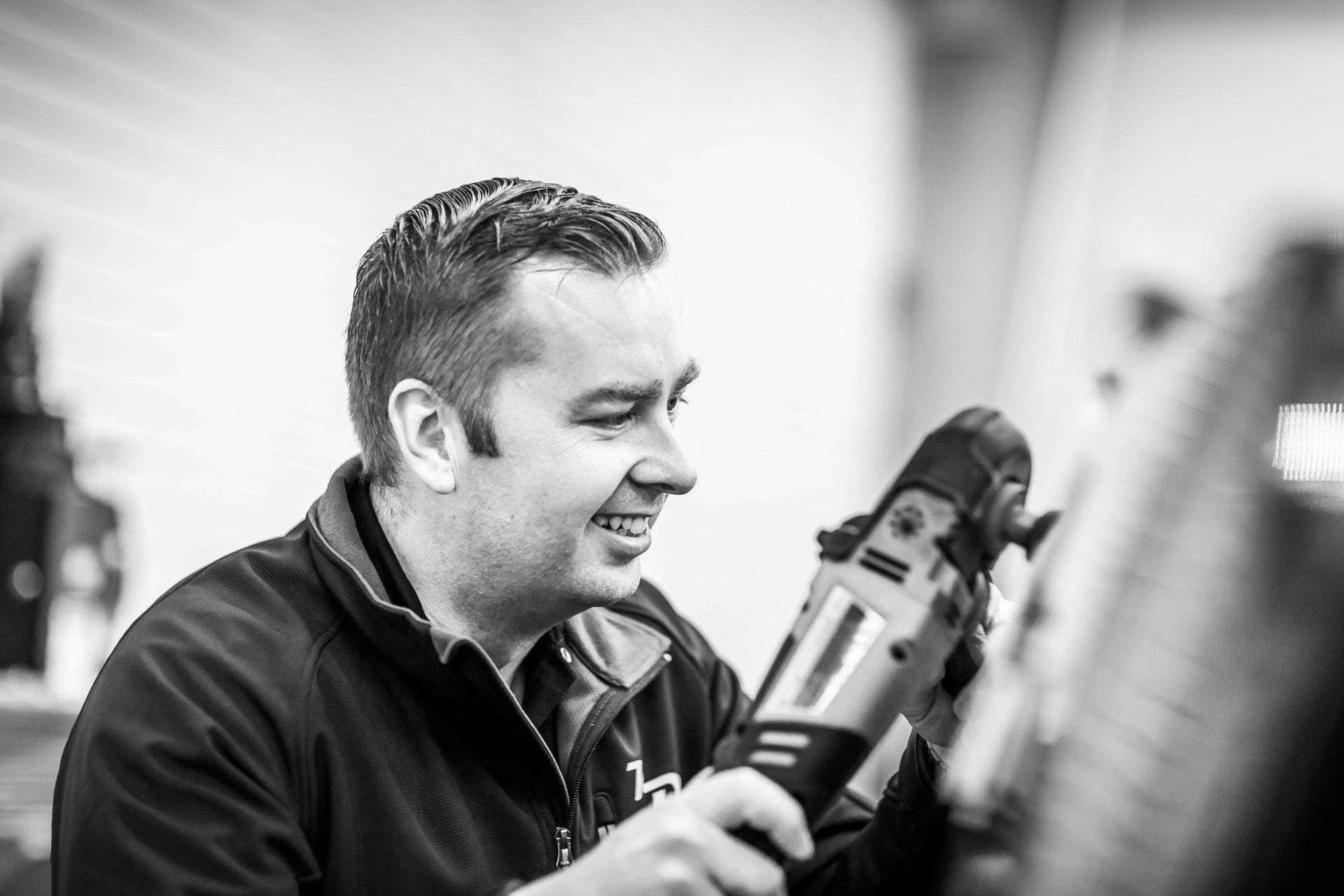 A man is holding a drill and smiling in a black and white photo.