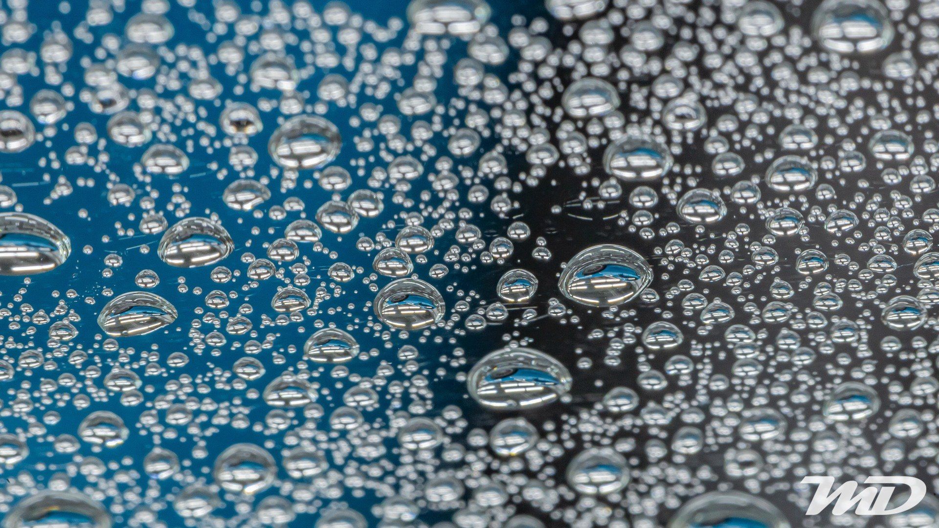 A close up of water drops on a blue and black surface.