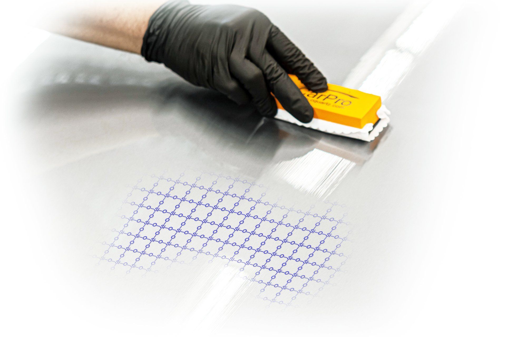 A person wearing black gloves is cleaning a car with a yellow sponge.