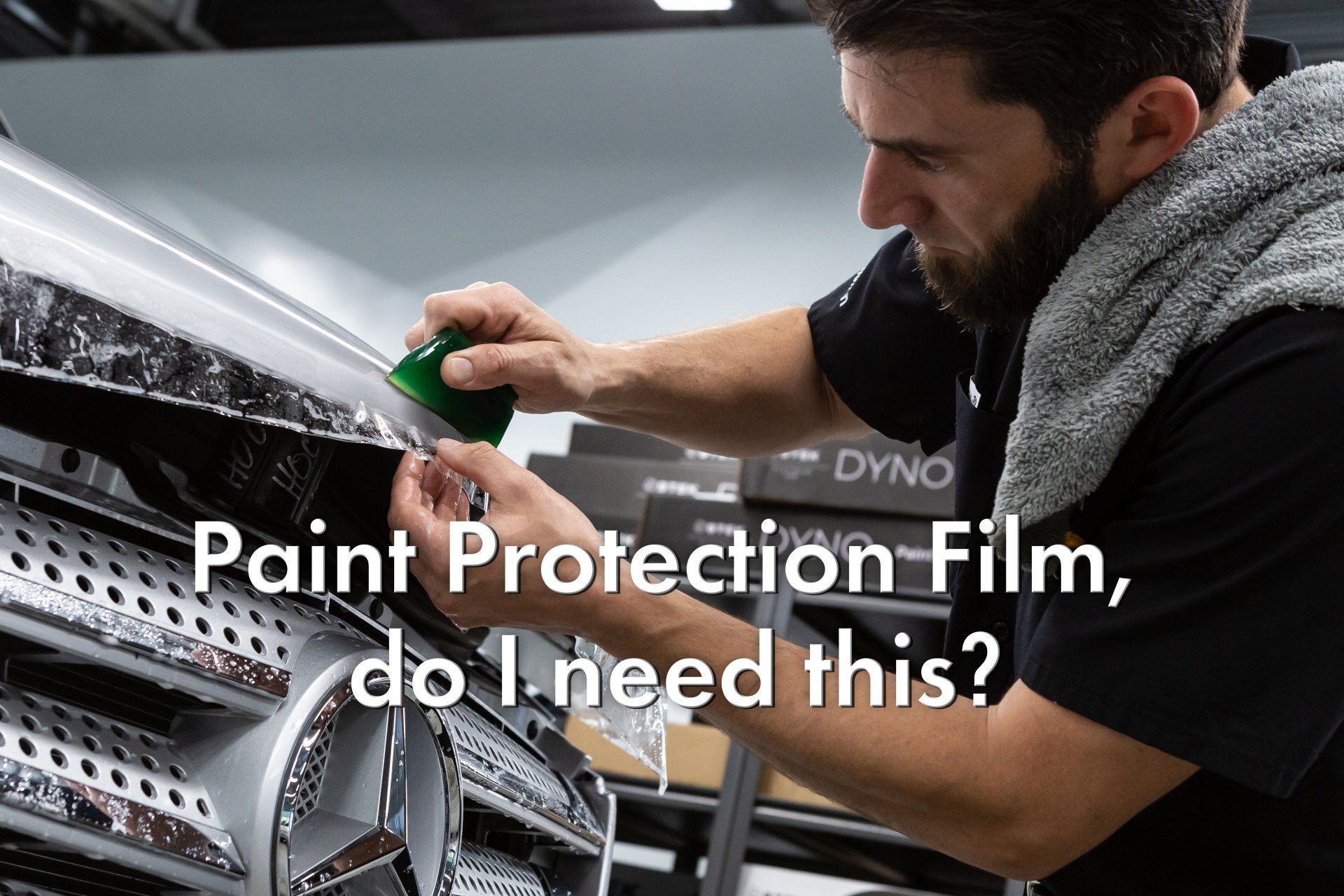 A man is applying paint protection film to the hood of a car.