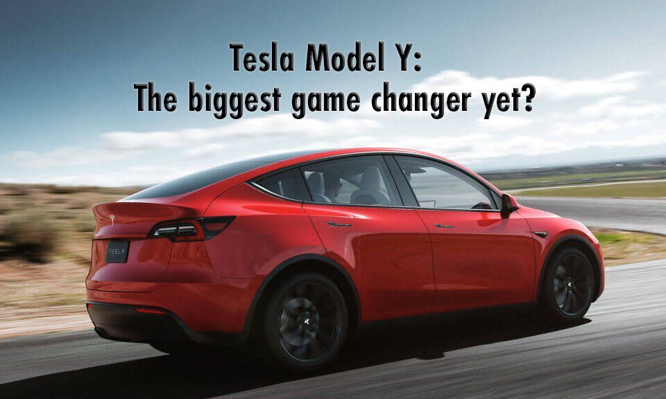 A red tesla model y is driving down a road.