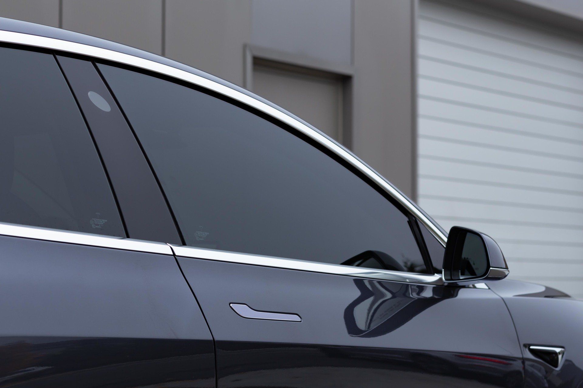 A close up of a tesla model 3 parked in front of a garage door.