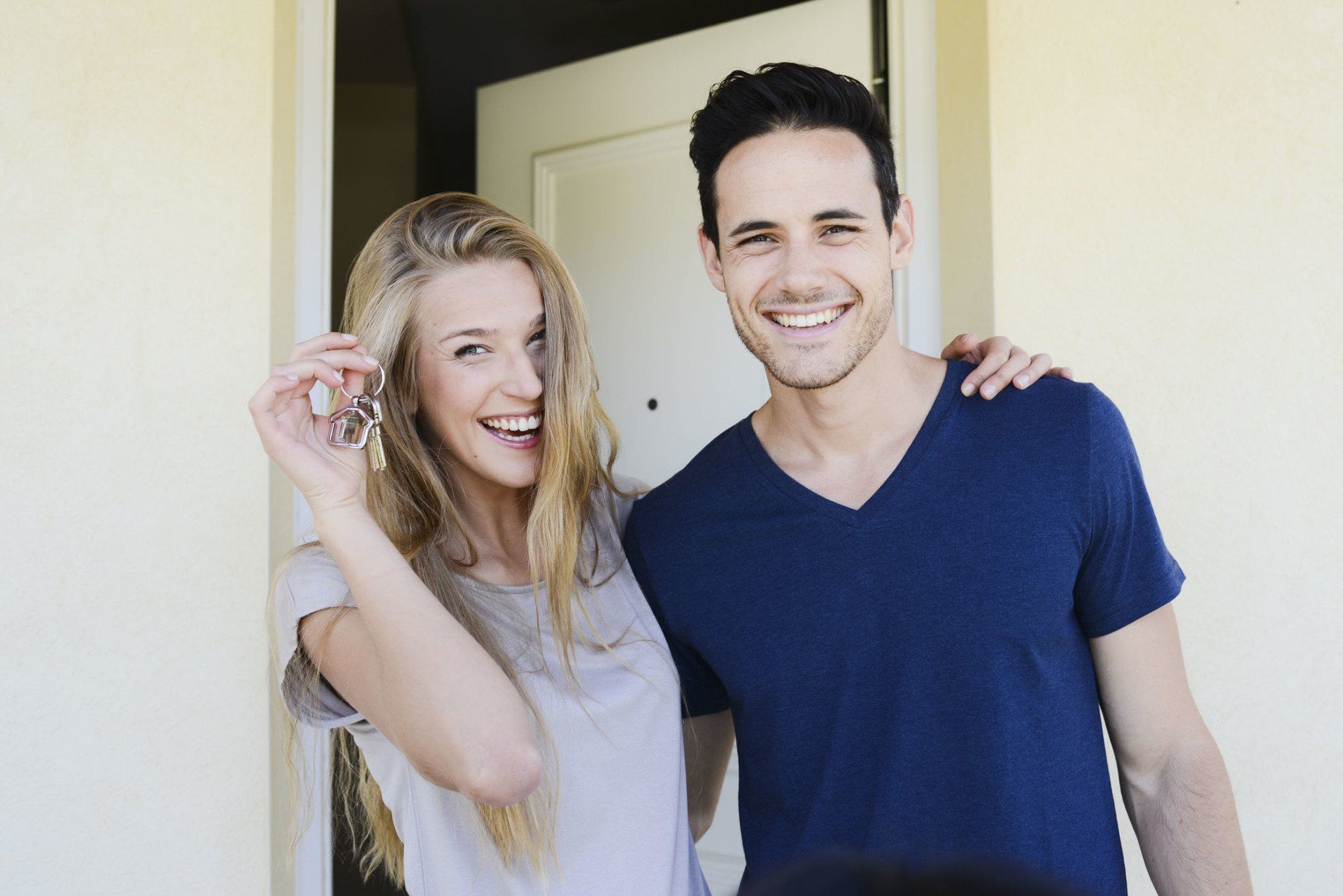 happy couple handing home keys in front of house door